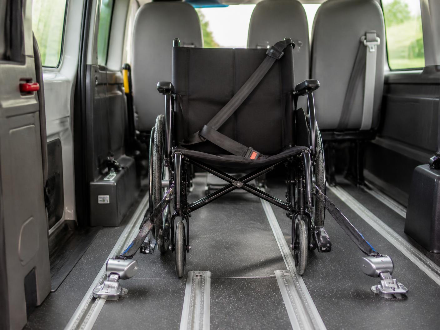 Inside a clean accessible van: a manual wheelchair anchored to floor tracks with four retractor straps and a shoulder belt.